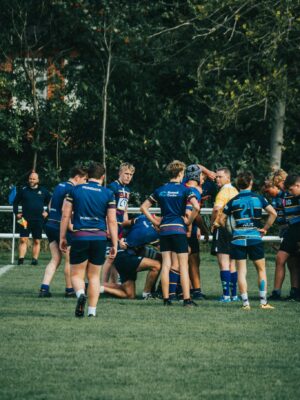 Rugby players huddle on a grassy field, preparing for the next play during a team sport match.