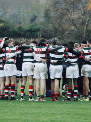 Rugby players in striped jerseys huddle during a game on an autumn field.